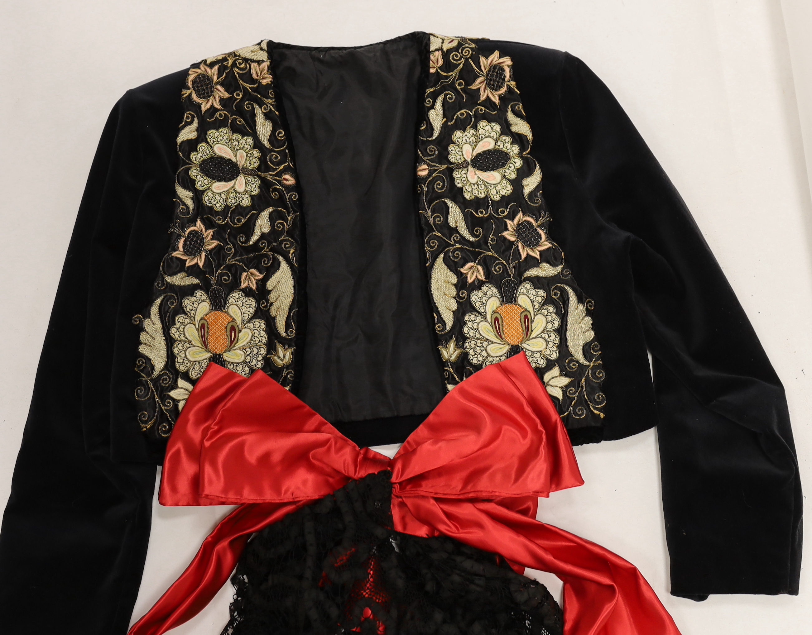 A velvet bolero with ornate polychrome silk embroidered and beaded panels, together with a full length black tape lace evening skirt (some damage) with red satin waisted sash